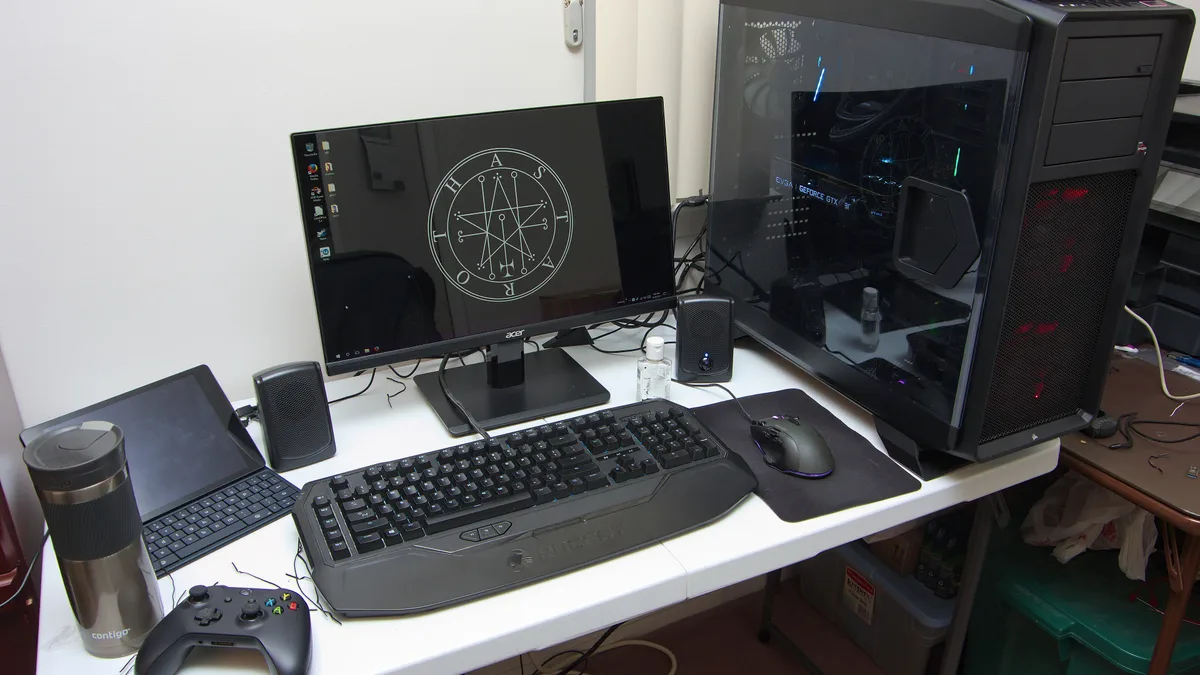 A desk gaming setup with a monitor, mechanical keyboard, gaming mouse, speakers and a controller next to a desktop PC