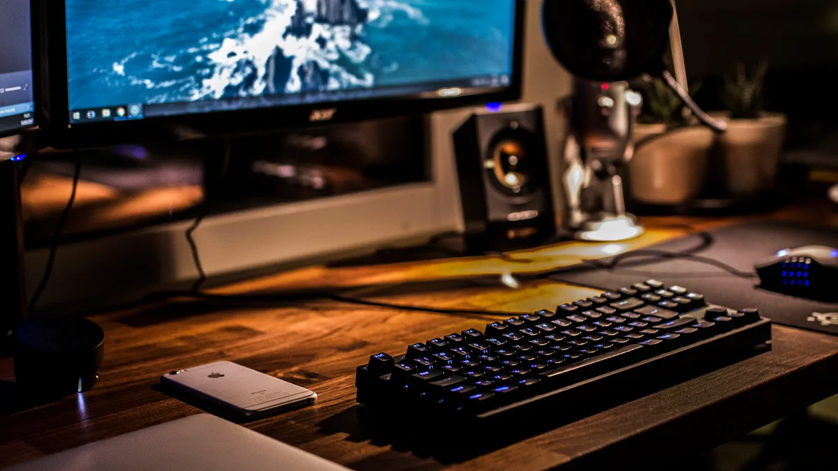A modest desktop gaming setup with a monitor, mechanical keyboard and speakers on a wooden desk